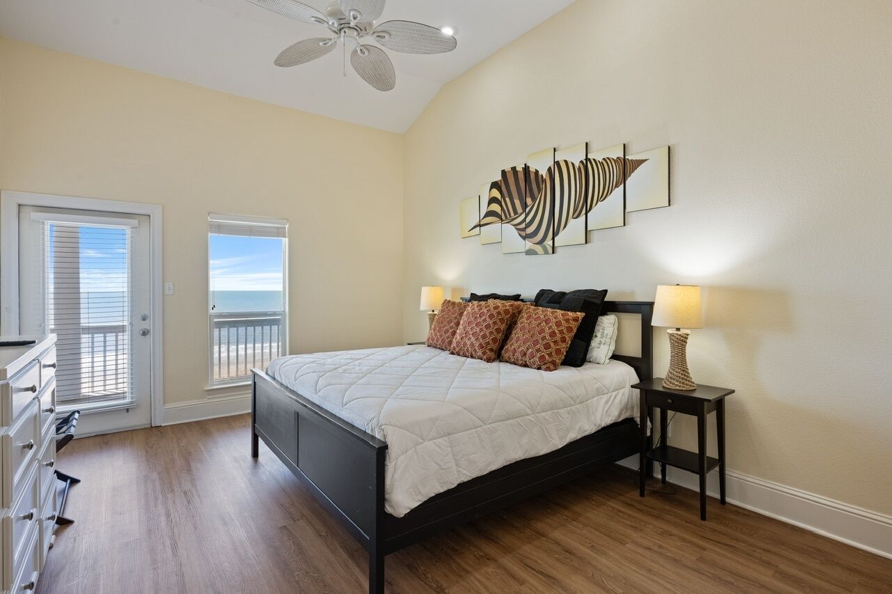A bedroom with a bed, two bedside lamps, a ceiling fan, and artwork on the wall.