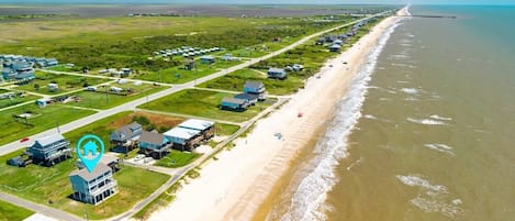 Vista aérea de uma área costeira com praia, casas e um píer.