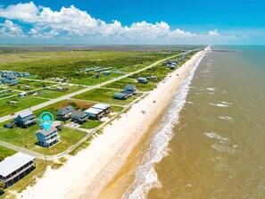 An aerial view of a coastal area with a beach, houses, and a pier. - Kiki Beach 4 Bedroom Home (Port Bolivar)