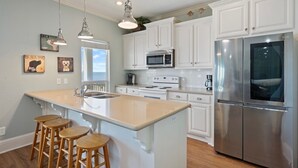 A kitchen with white cabinets, stainless steel appliances, and wooden bar stools. - Kiki Beach 4 Bedroom Home (Port Bolivar)