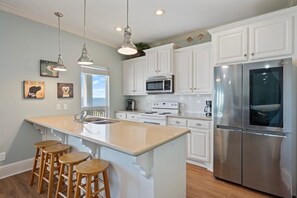 A kitchen with white cabinets, stainless steel appliances, and wooden bar stools. - Kiki Beach 4 Bedroom Home (Port Bolivar)