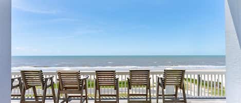 Una terraza de madera con cuatro sillas frente a una vista de la playa.