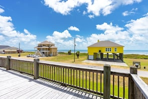 A coastal property with a wooden deck, a yellow building, and a two-story structure with a balcony. - Beachy Keen 3 Bedroom Home (Port Bolivar)