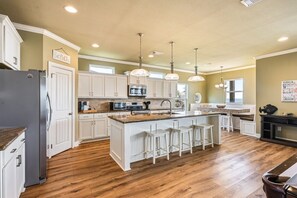 A kitchen with white cabinetry, a central island with stools, a refrigerator, and a microwave. - Beachy Keen 3 Bedroom Home (Port Bolivar)