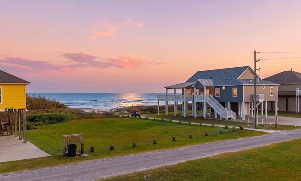 A coastal property with a covered outdoor area, a grassy lawn, and a road leading to the beach. - Beachy Keen 3 Bedroom Home (Port Bolivar)