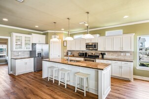 A kitchen with white cabinets, a central island with stools, stainless steel appliances, and pendant lighting.