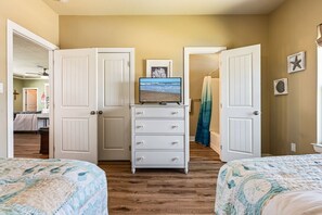 A bedroom with two beds, a dresser, a television, and a view of a beach through the window. - Beachy Keen 3 Bedroom Home (Port Bolivar)