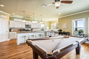 A pool table in a room with wooden flooring, white cabinets, and pendant lighting. - Beachy Keen 3 Bedroom Home (Port Bolivar)