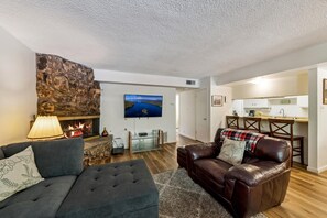 A living room with a stone fireplace, a television mounted on the wall, a sofa, and a leather armchair. - 1168hc 3 Bedroom Condo (South Lake Tahoe)