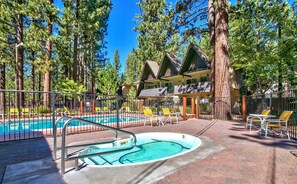 A pool area with a hot tub, surrounded by a fence, and a building with a sloped roof in a forested setting. - 1168hc 3 Bedroom Condo (South Lake Tahoe)