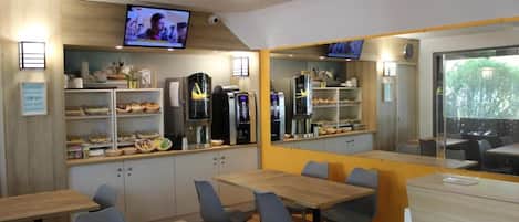 Un área de cocina moderna con electrodomésticos integrados, un televisor montado en la pared y una zona de estar con mesas y sillas.