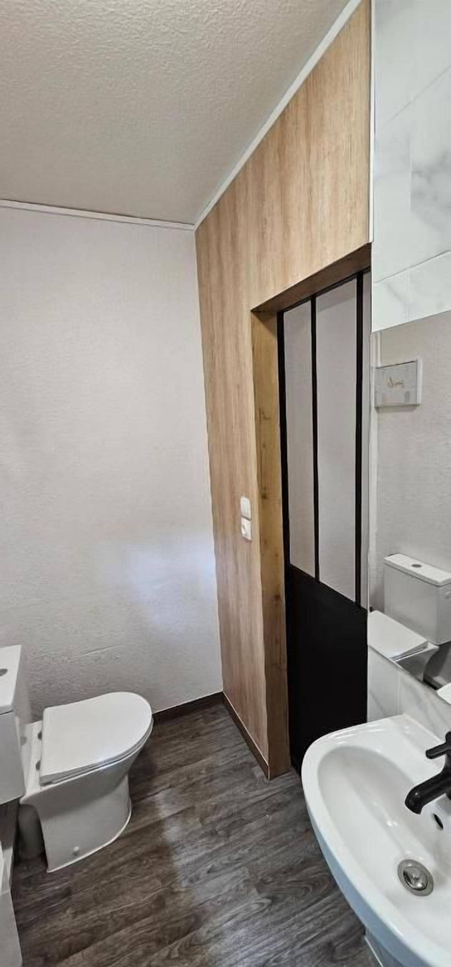 A compact bathroom with a toilet, sink, and wooden paneling.