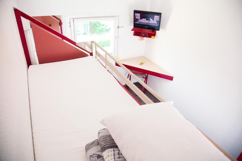 Una habitació amb llit, escriptori, televisió i finestra.