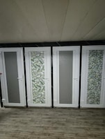 Cuatro puertas con paneles de vidrio esmerilado, suelo de madera y pared negra.