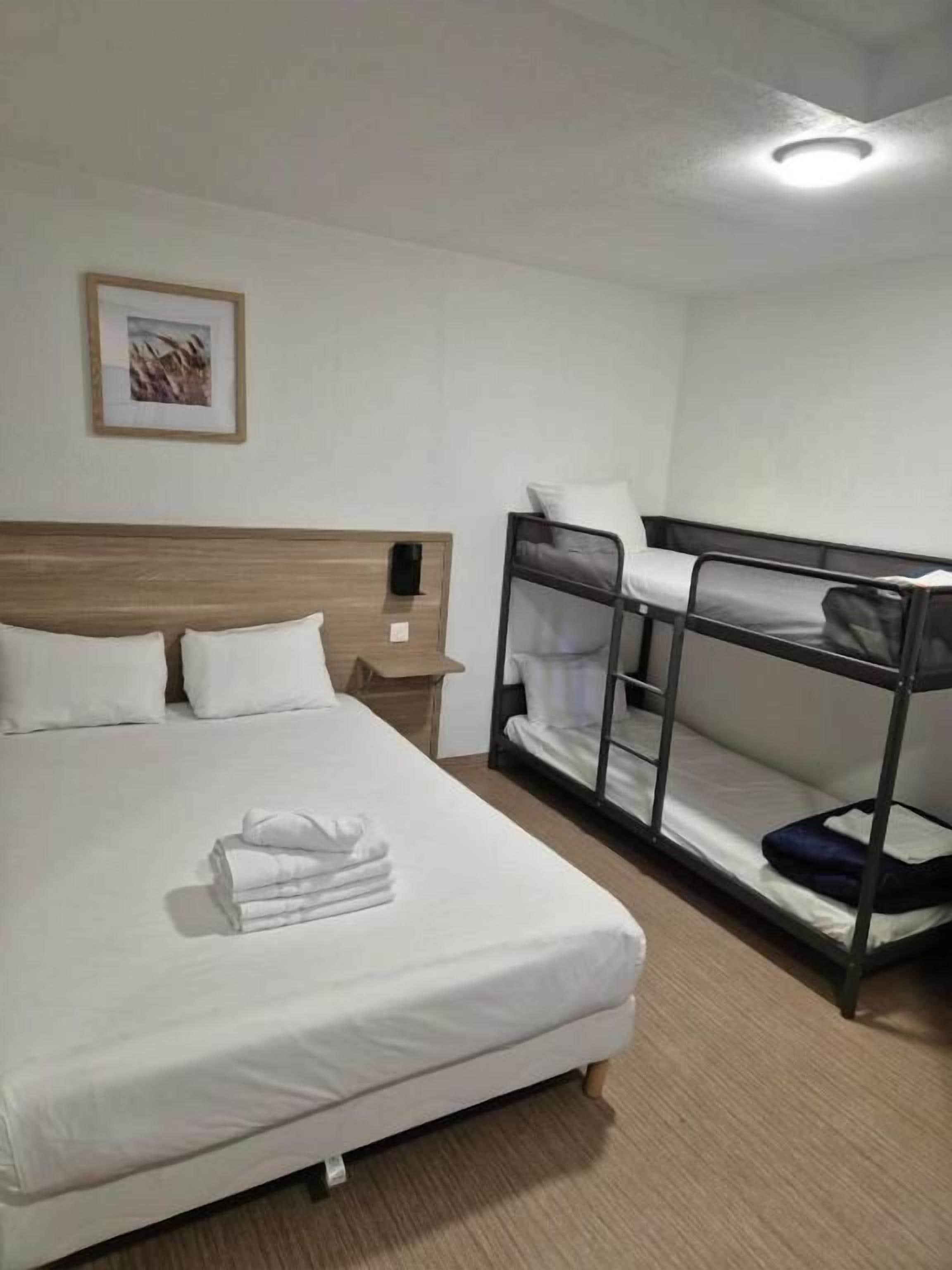 A hotel room with a single bed, a bunk bed, a bedside table, and a framed picture on the wall.