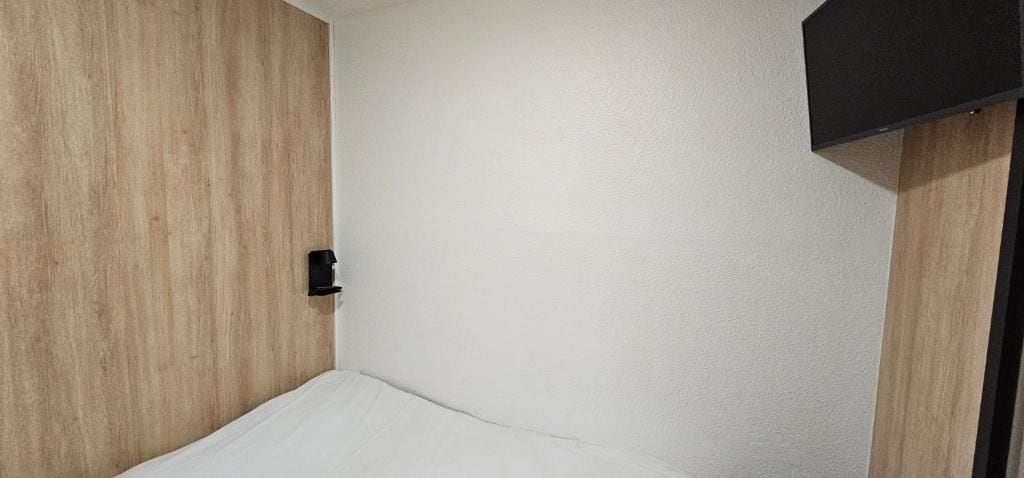 Una habitación con pared de madera, un colchón blanco y un objeto negro en la pared.