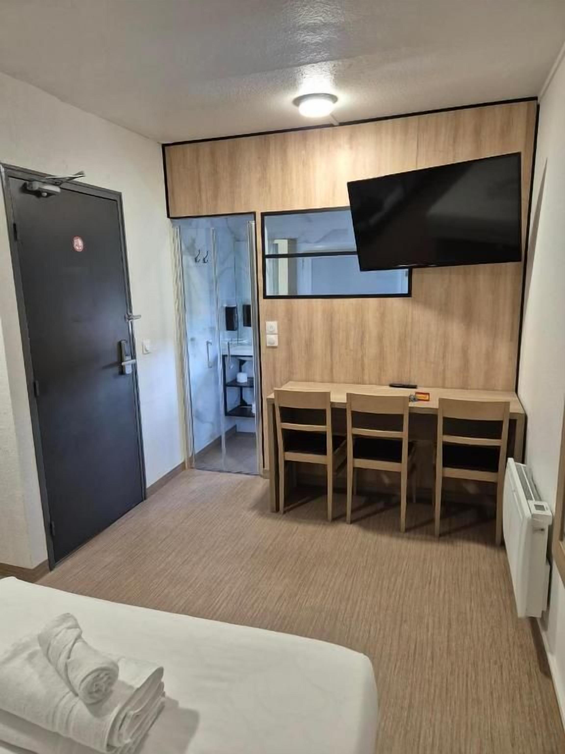 A hotel room with a bed, a desk with chairs, a flat-screen TV mounted on the wall, and a door leading to a bathroom.