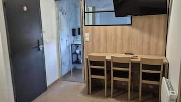 A hotel room with a bed, a desk with chairs, a flat-screen TV mounted on the wall, and a door leading to a bathroom.