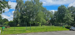 A fenced outdoor area with trees and a parking lot.