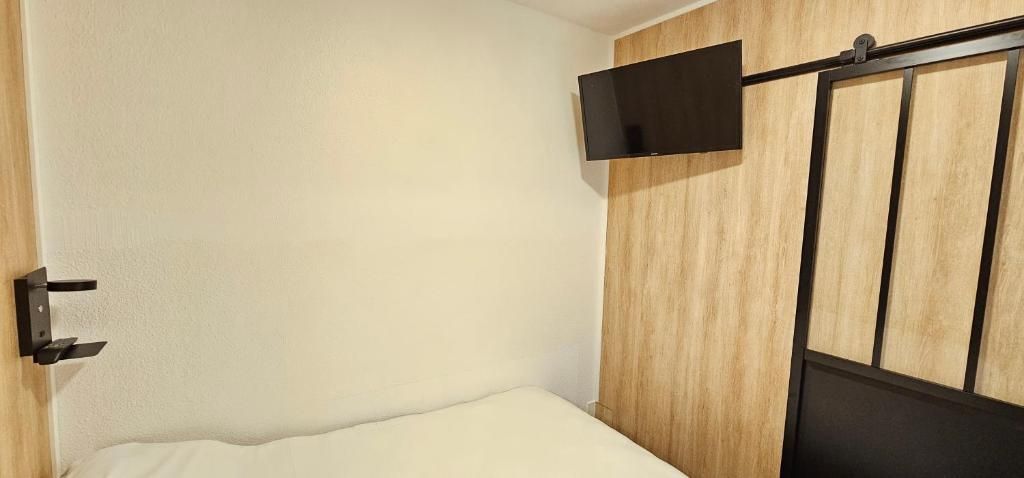 A room with a bed, a mounted television, and a wooden panel wall.