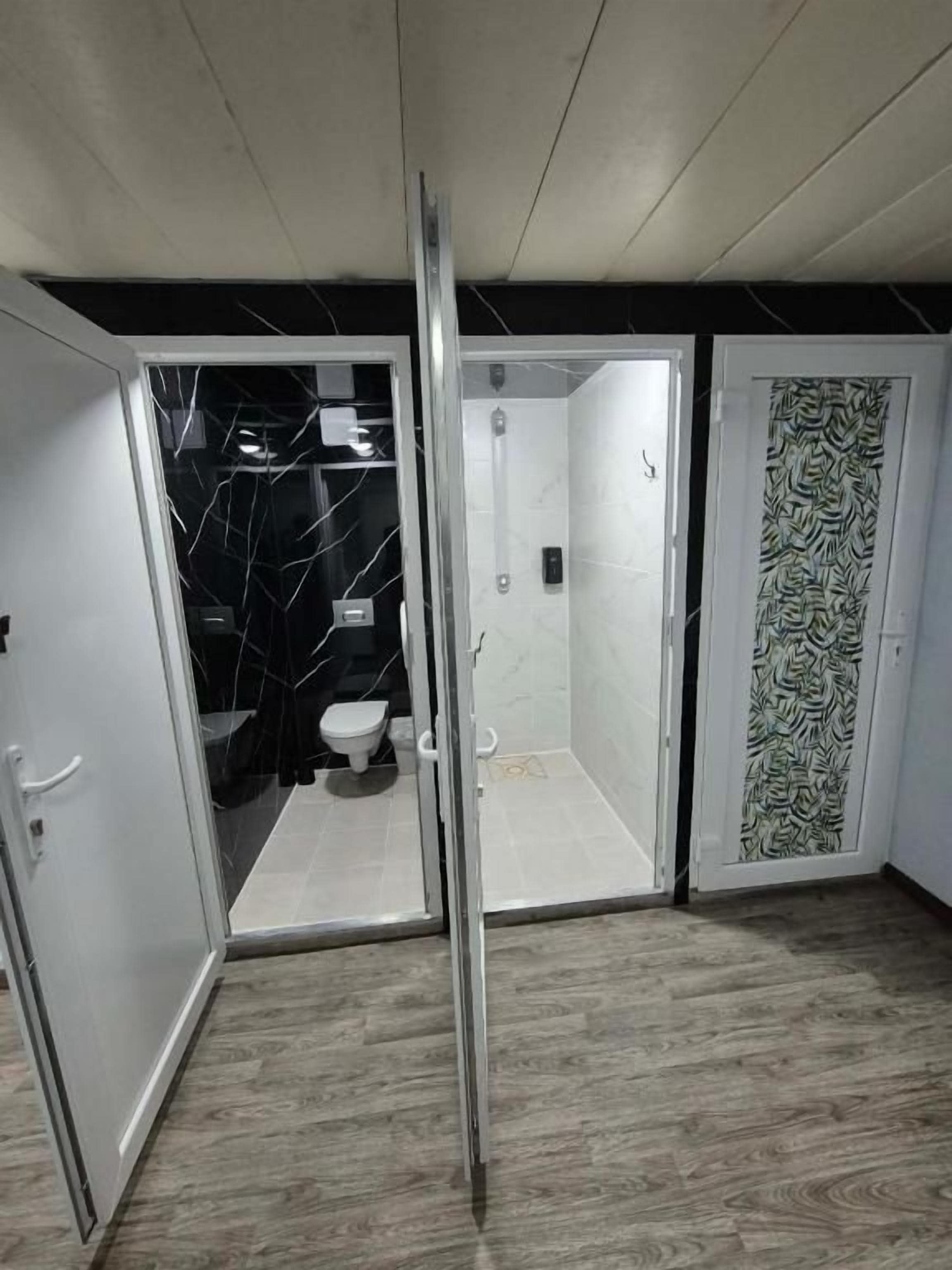Casa de banho com chuveiro, sanita e porta de vidro para a área do chuveiro.