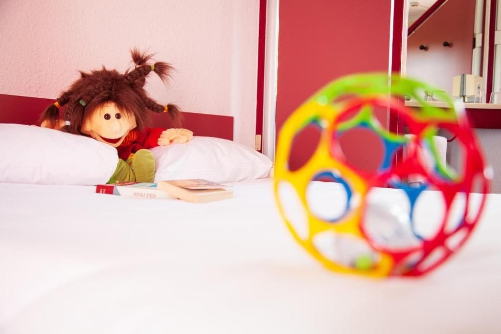 Quarto com uma cama, uma boneca e um brinquedo de bola colorido.