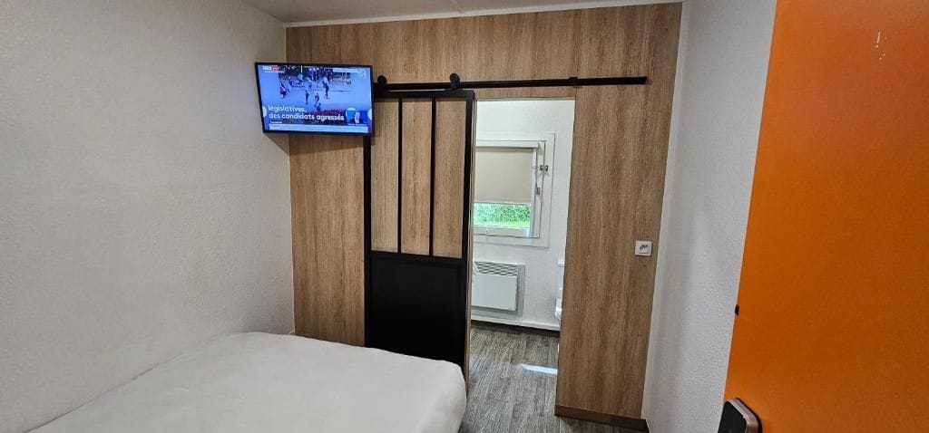 A hotel room with a bed, a television mounted on the wall, and a sliding door leading to a bathroom.