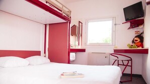 Una cama individual con almohadas, un escritorio con silla, un televisor y una ventana.