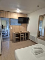 Una habitación de hotel con cama, escritorio y sillas, televisor de pantalla plana y espejo.