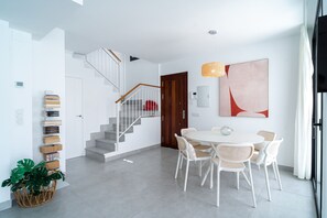 A modern interior with a staircase, a dining area with white chairs, and a large abstract painting. - Villa Casa Mezcal by Casasol (Nerja)