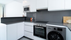 A compact kitchen with a built-in microwave, oven, and washing machine, featuring white cabinetry and a grey countertop. - Villa Casa Mezcal by Casasol (Nerja)