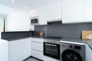 A compact kitchen with a built-in microwave, oven, and washing machine, featuring white cabinetry and a grey countertop. - Villa Casa Mezcal by Casasol (Nerja)