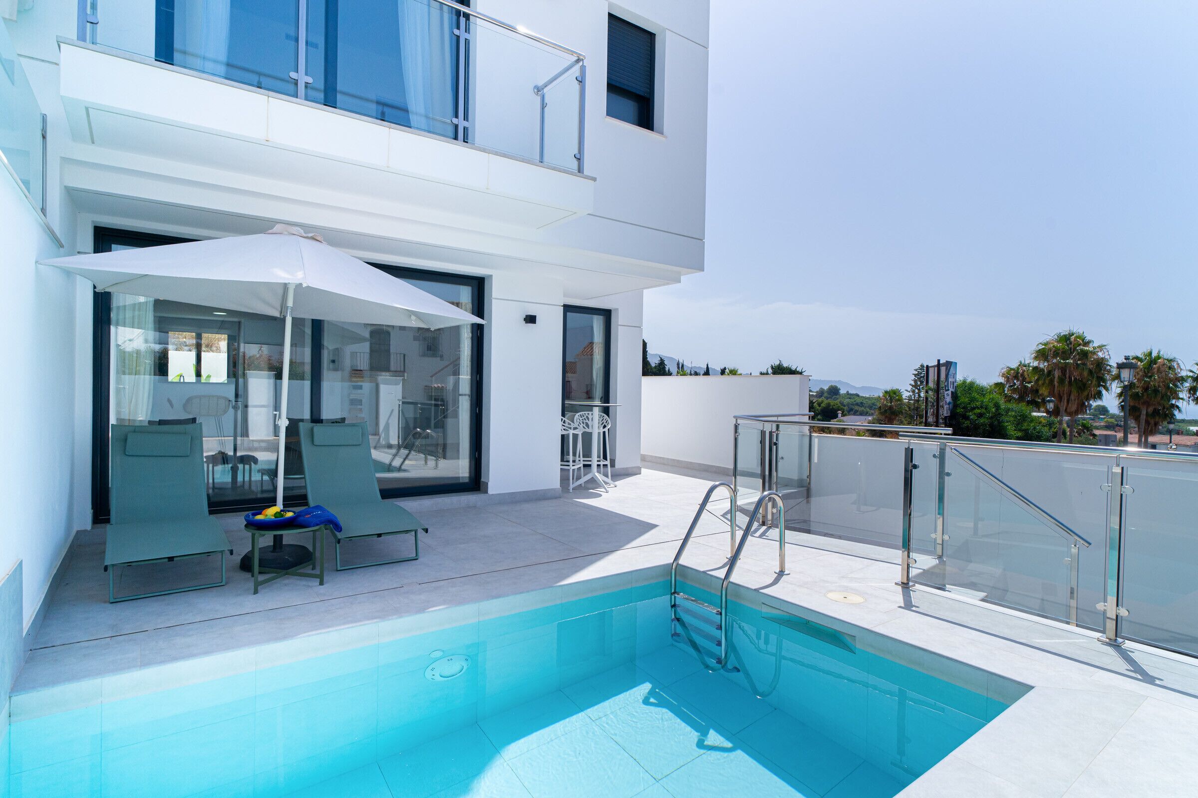 Un área de piscina moderna al aire libre con sillones de descanso y barandilla de vidrio.