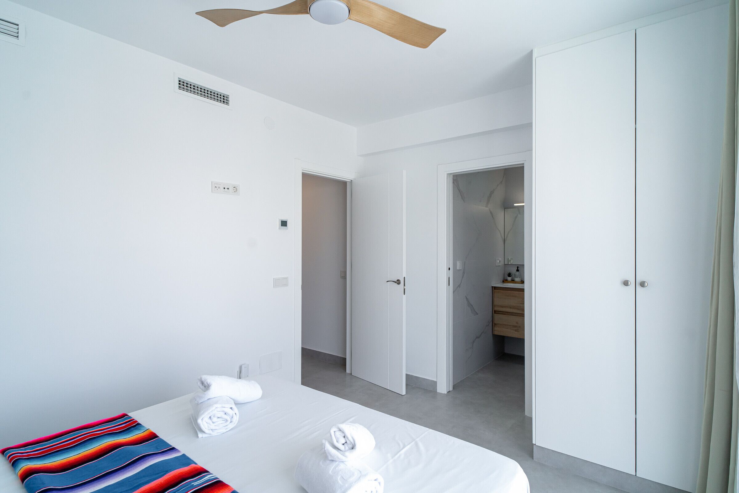 Habitación de hotel con cama, ventilador de techo, baño con espejo y armario.