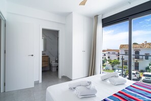 A hotel room with a large bed, a bathroom with a toilet and sink, and a view of the street and buildings outside. - Villa Casa Mezcal by Casasol (Nerja)