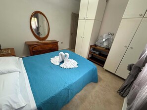Un dormitorio con cama, cómoda, espejo, armario y ventilador.