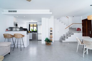 A modern kitchen with a central island, bar stools, a dining area with a white table and chairs, and a staircase leading to another level. - Villa Casa Mezcal by Casasol (Nerja)