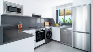 A modern kitchen with stainless steel appliances, a built-in oven, a washing machine, and a window with a view of greenery. - Villa Casa Mezcal by Casasol (Nerja)