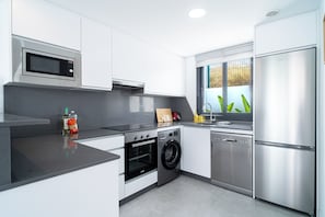 A modern kitchen with stainless steel appliances, a built-in oven, a washing machine, and a window with a view of greenery. - Villa Casa Mezcal by Casasol (Nerja)