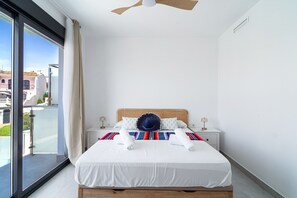 A modern hotel room with a large bed, a ceiling fan, and a balcony with a view of buildings. - Villa Casa Mezcal by Casasol (Nerja)
