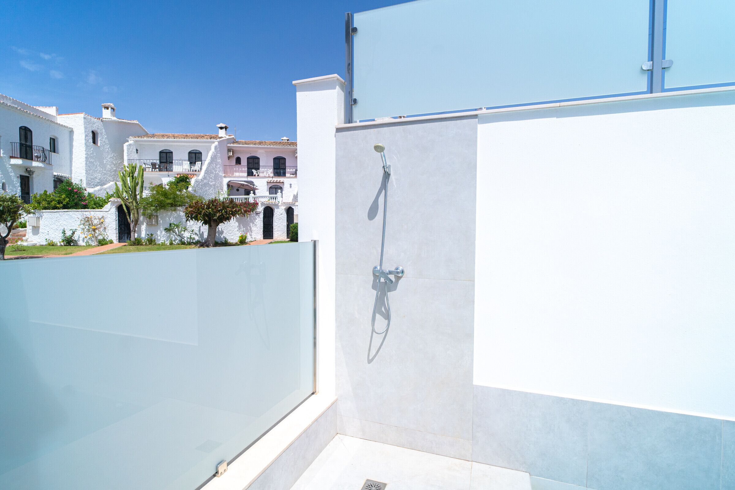 A modern bathroom with a shower, a white exterior wall, and a view of traditional buildings in the background.
