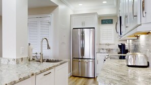 A modern kitchen with white cabinetry, a stainless steel refrigerator, a marble countertop, and a coffee maker. - Summit 908/908A Luxury Gulf-View Escape | TOPS'L Resort | Walk to the Beach (Miramar Beach)