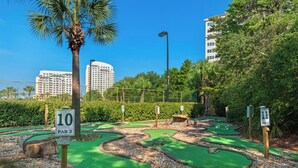 A miniature golf course with numbered holes, surrounded by greenery and palm trees. - Summit 908/908A Luxury Gulf-View Escape | TOPS'L Resort | Walk to the Beach (Miramar Beach)