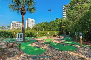 A miniature golf course with numbered holes, surrounded by greenery and palm trees. - Summit 908/908A Luxury Gulf-View Escape | TOPS'L Resort | Walk to the Beach (Miramar Beach)