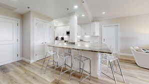 Una cocina moderna con armarios blancos, encimera de mármol y taburetes de bar.
