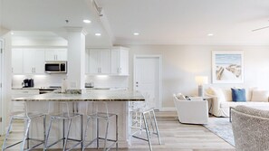 A modern kitchen with white cabinets, a marble countertop, and stainless steel appliances. There is a dining area with a white sofa and a lamp. - Summit 908 – Spacious Gulf-View Retreat at TOPS'L (Miramar Beach)