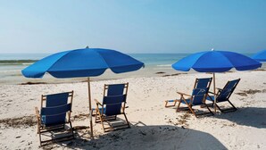 Una playa con sombrillas azules y sillas de madera.