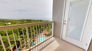 A balcony with a view of a pool and greenery, a door with a screen, and a clear sky. - Summit 908 – Spacious Gulf-View Retreat at TOPS'L (Miramar Beach)