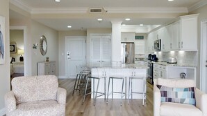 Una cocina amplia con muebles blancos, una isla central con taburetes y un comedor con sofá estampado.
