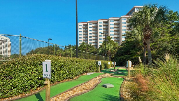 A miniature golf course with numbered holes, surrounded by hedges and palm trees, with a building in the background. - Summit 0908A Romantic Gulf-View Studio at TOPS'L Resort (Miramar Beach)